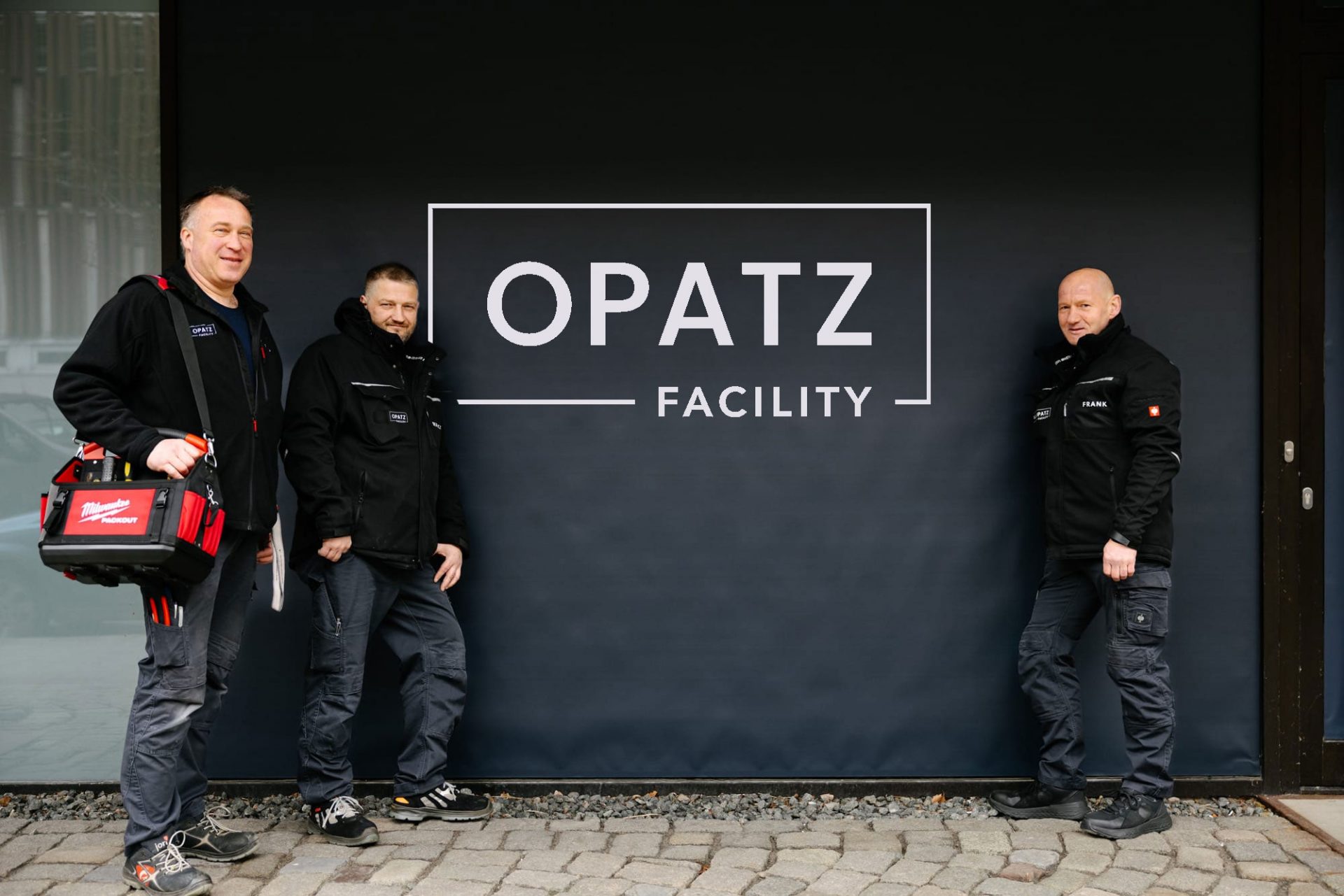 Die Facility Manager im Einsatz © OPATZ Group. Die Facility Manager der OPATZ Group vor einer Wand mit dem Logo.